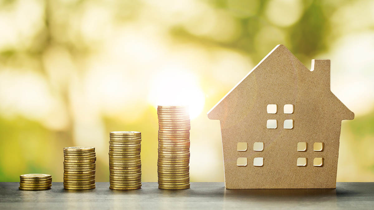 Cardboard house next to stacks of coins